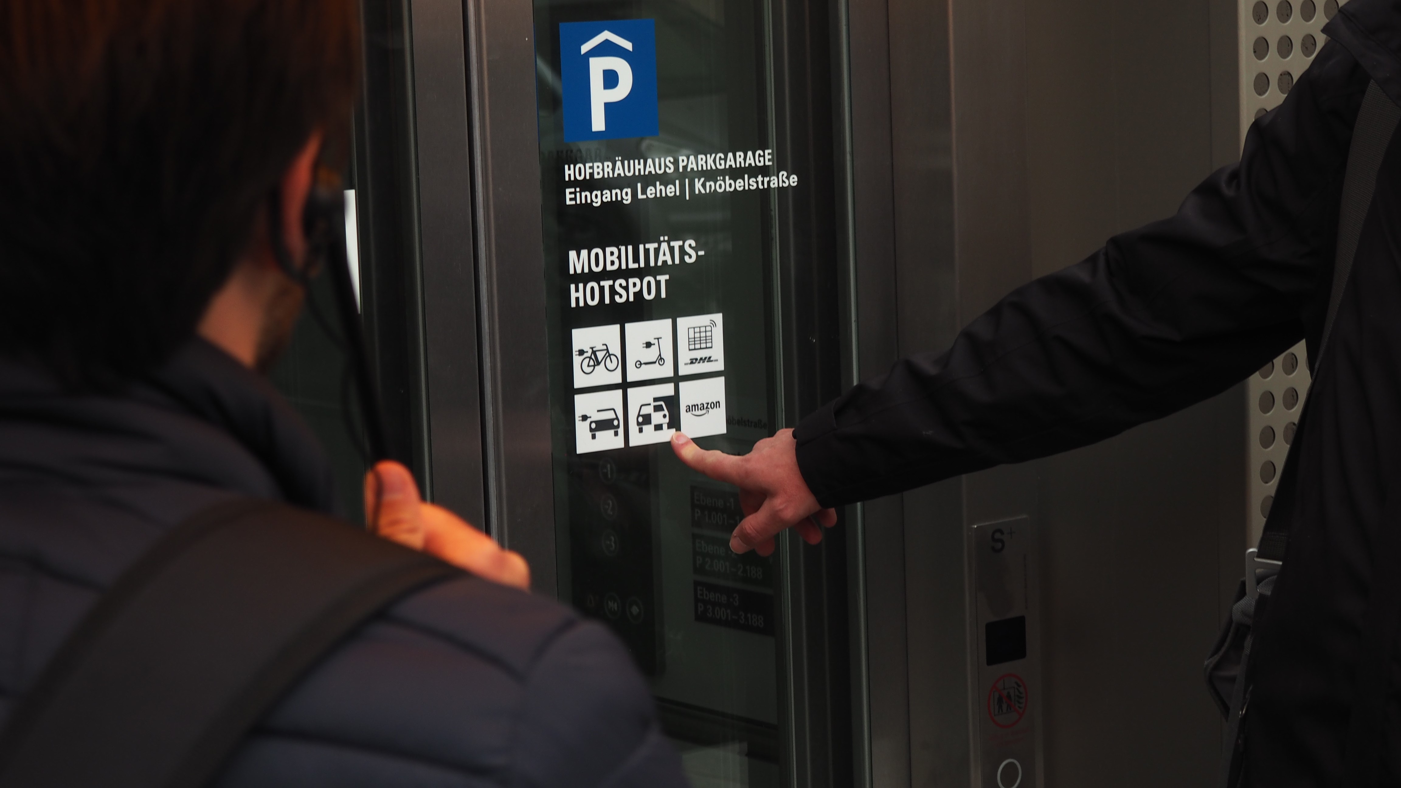 Ein Finger zeigt auf Mobilitätssymbole an einer Scheibes eines Aufzugs.